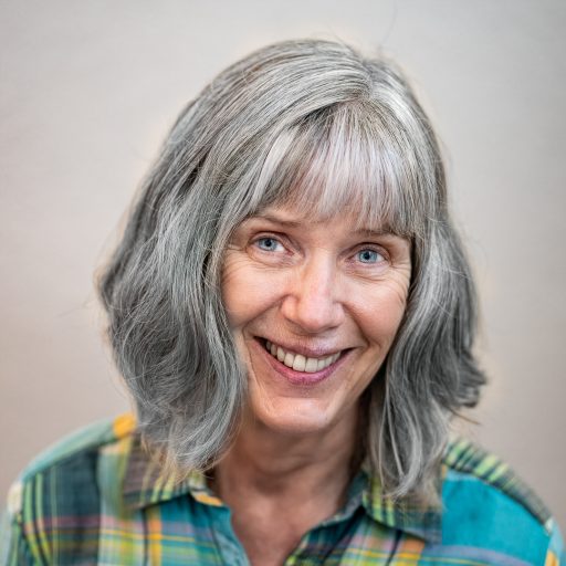 Portrait of Nicolle Goldman, plaid shirt, silver hair, big smile